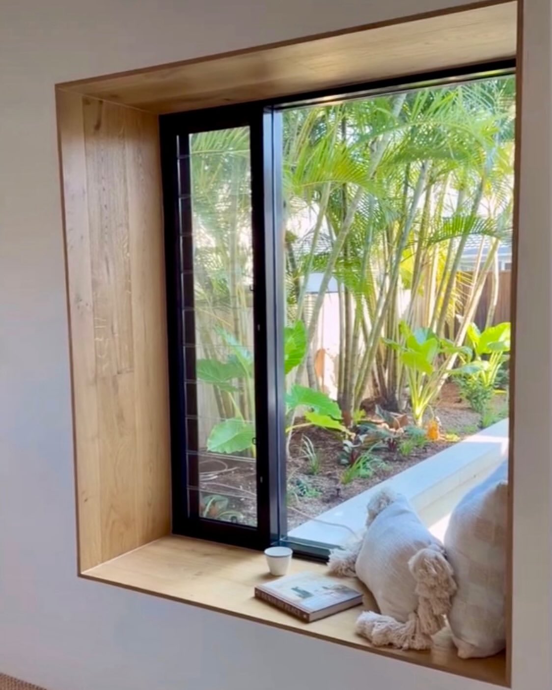Black aluminium picture window in a timber reveal looking onto a subtropical garden